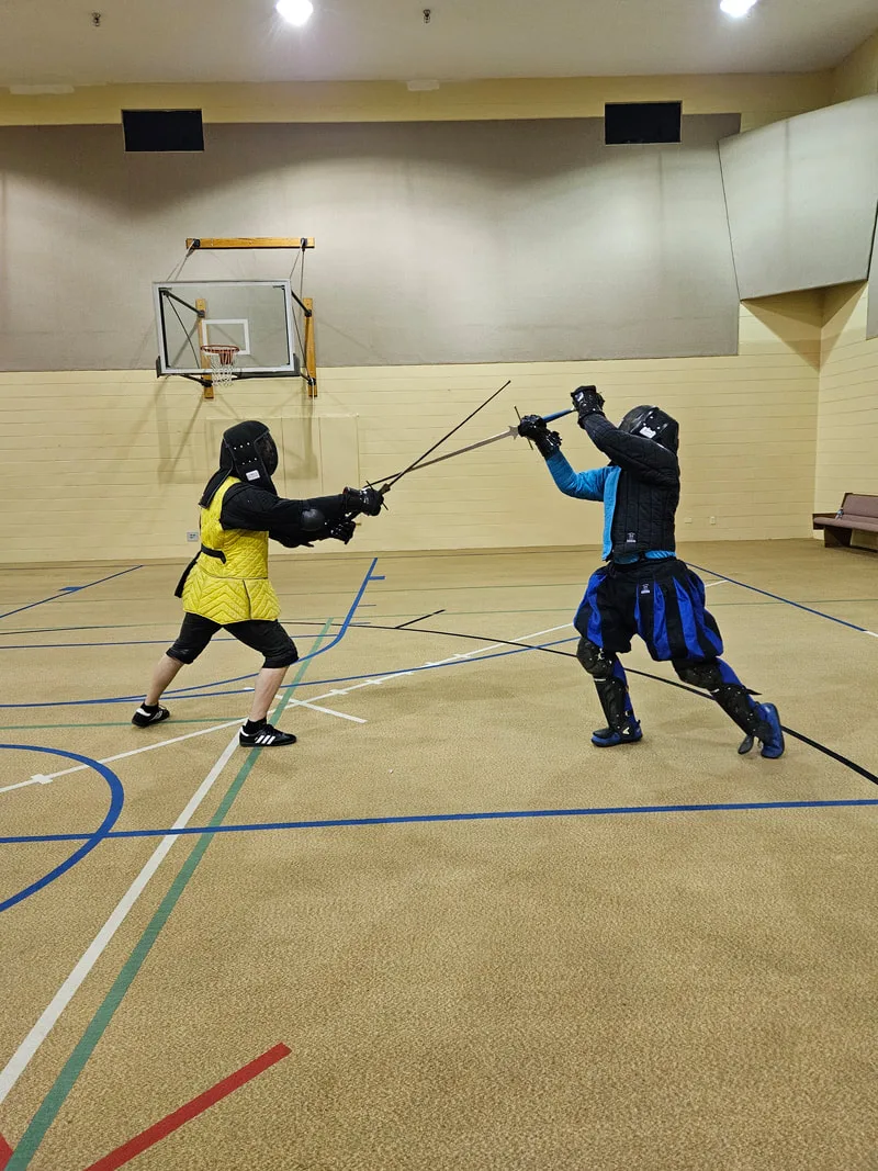 Ryan and an adult student engaged in a longsword fight.