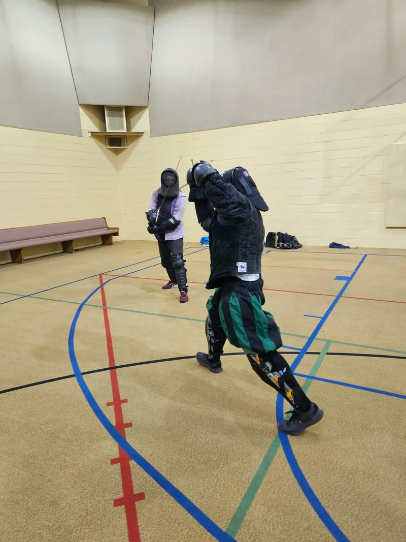 Chris and an adult student engaged in a longsword fight.